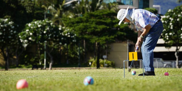 Gateball player Steven Kaneshiro strikes a ball toward the first gate during practice Wednesday, Sept. 4, 2024, at Ala Moana Beach Park in Honolulu. Kaneshiro discovered the sport after re-connecting with Art Kimura. Kimura was one of Kaneshiro’s high-school teachers. (Kevin Fujii/Civil Beat/2024)