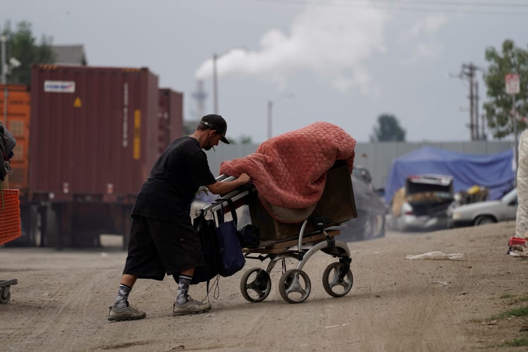 A man pushing a shopping cart in front of shipping containers