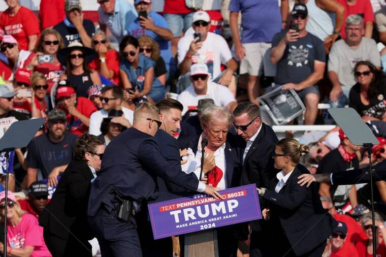 BRENDAN McDERMID / REUTERS
                                Republican presidential candidate and former President Donald Trump is assisted by U.S. Secret Service personnel after he was grazed in the ear by a bullet during a campaign rally at the Butler Farm Show in Butler, Pennsylvania,Saturday.