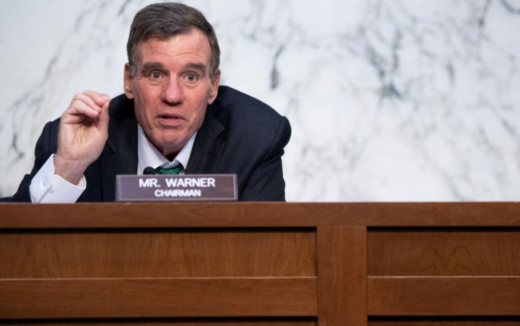 Mark Warner in front of sign saying Chairman Mr. Warner