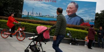 People walk past a poster of late Chinese leader Deng Xiaoping, who launched the country on its