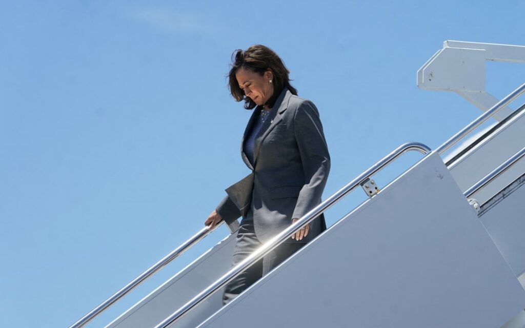 Kamala Harris walking down a stairway from a plane dressed in gray