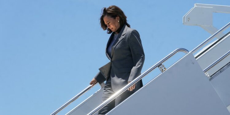 Kamala Harris walking down a stairway from a plane dressed in gray