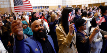 About 200 people wave American flags after being sworn in at a naturalization ceremony in Boston on April 17, 2024. (Danielle Parhizkaran/The Boston Globe via Getty Images)