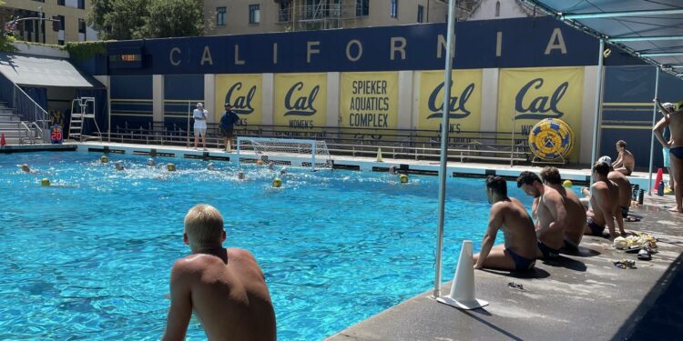 Multiple people sit with their feet in the water at a pool.