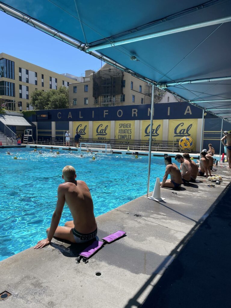 Multiple people sit with their feet in the water at a pool.