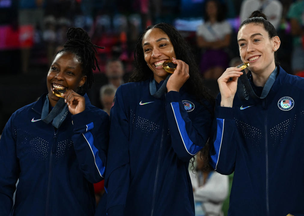 Gold medallists (From L) USA's #08 Chelsea Gray, USA's #09 A'ja Wilson and USA's #10 Breanna Stewart bite their medal as they celebrate on the podium after the women's Gold Medal basketball match between France and the USA during the Paris 2024 Olympic Games at the Bercy  Arena in Paris on August 11, 2024. (Photo by Paul ELLIS / AFP) (Photo by PAUL ELLIS/AFP via Getty Images)