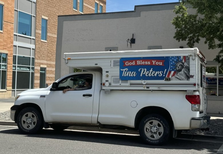 A white pickup truck with a red, white and blue banner affixed to a camper shell. The banner, which features the Statue of Liberty, reads 