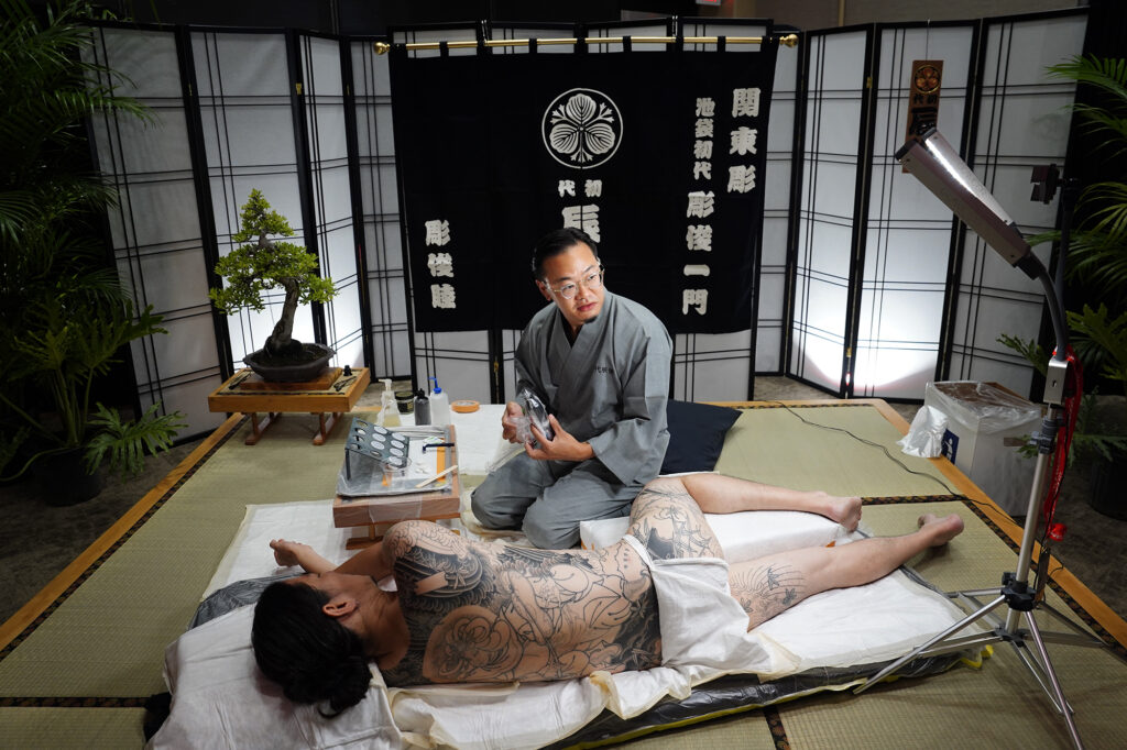 Tatsutoshi tattoos a client at The Hawaii Tattoo Expo Friday, Aug. 2, 2024, in Honolulu. Tatsutoshi whose name is Ryoma Uno, uses a traditional Japanese style form of tattooing done by hand. (Kevin Fujii/Civil Beat/2024)