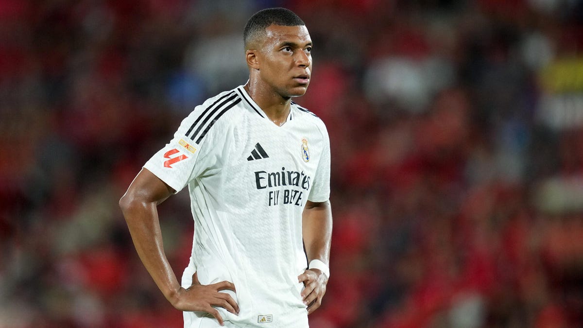 Real Madrid player Kylian Mbappe standing with his hands on his hips, looking upwards.