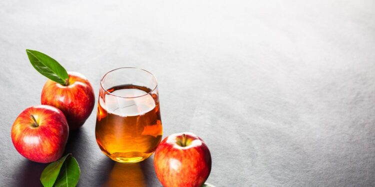 Apple juice in a glass and a jug accompanied by red apples