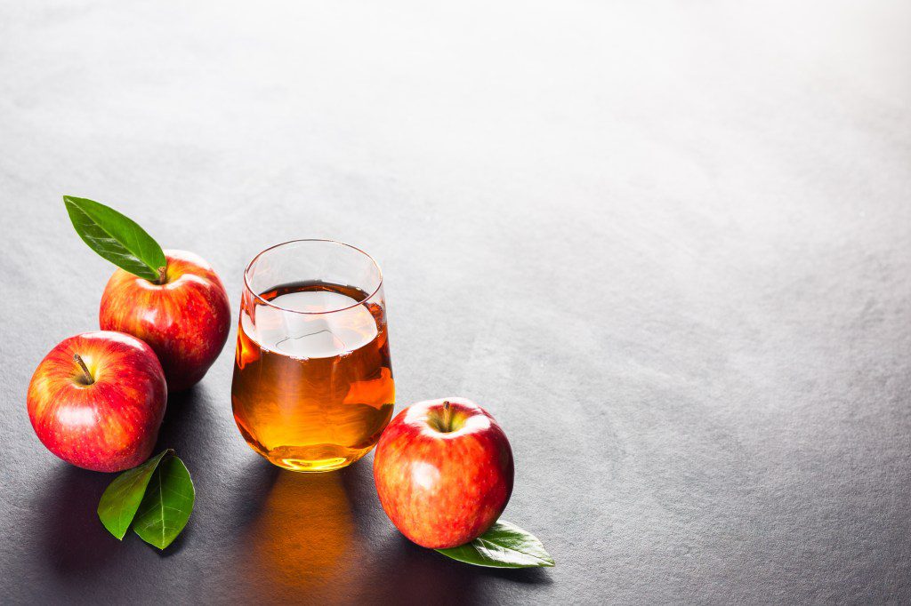 Apple juice in a glass and a jug accompanied by red apples