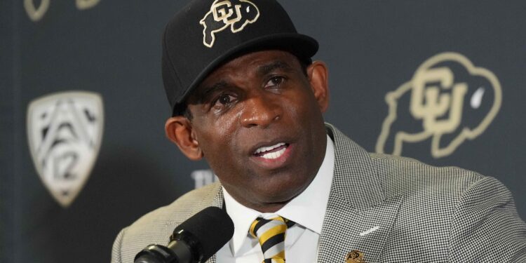 Deion Sanders in front of a microphone wearing a Colorado hat