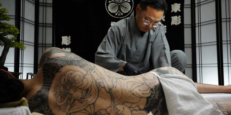 Tatsutoshi tattoos a client at The Hawaii Tattoo Expo Friday, Aug. 2, 2024, in Honolulu. Tatsutoshi whose name is Ryoma Uno, uses a traditional Japanese style form of tattooing done by hand. (Kevin Fujii/Civil Beat/2024)