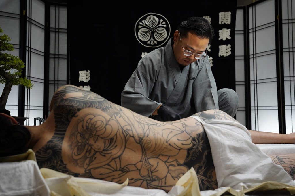 Tatsutoshi tattoos a client at The Hawaii Tattoo Expo Friday, Aug. 2, 2024, in Honolulu. Tatsutoshi whose name is Ryoma Uno, uses a traditional Japanese style form of tattooing done by hand. (Kevin Fujii/Civil Beat/2024)