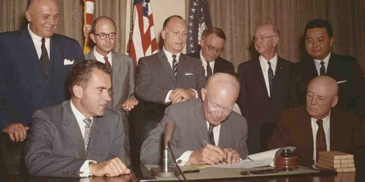 Dwight Eisenhower signing paper as Richard Nixon, and others look on