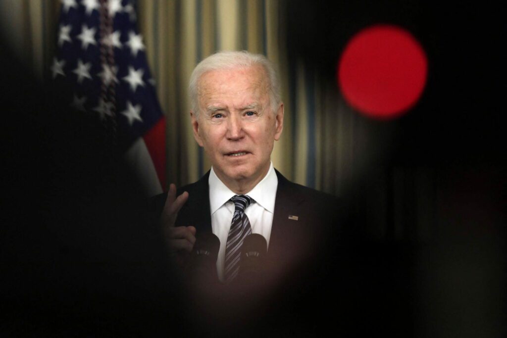 A white man speaks at a podium with American flags behind him