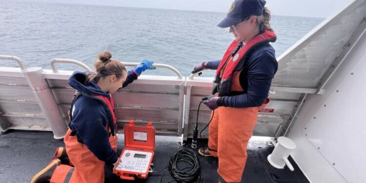 Elia Betschen, left, and Jessie Matthews, right, prepare to retrieve a passive acoustic monitor from the Gulf of Maine during a recent surveillance trip. (Courtesy of Jeff Nichols, Maine Department of Marine Resources via Maine Public)