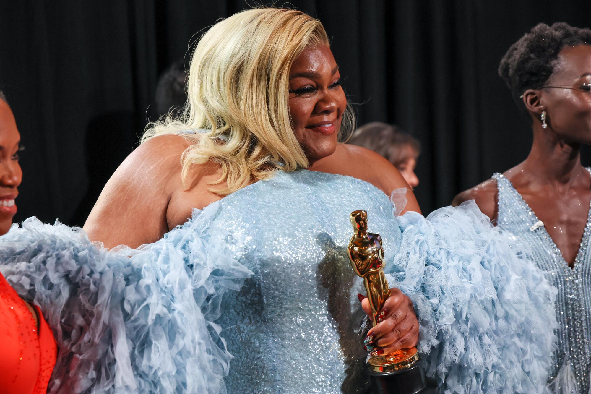 A blond-haired woman in a light blue gown holds an Oscar.