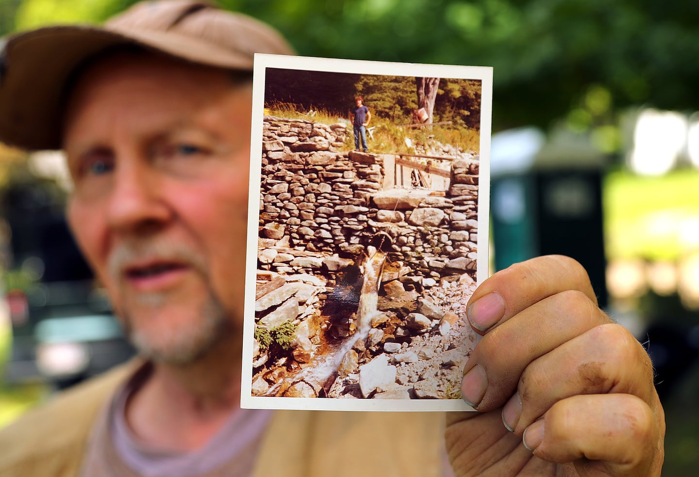 David Brown’s property abuts the dam where he has lived for nearly 50 years. He held a photo from 1980 of himself standing atop the dam. 