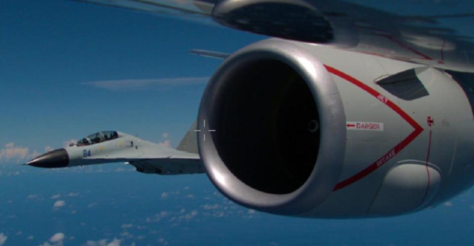 A Chinese jet passing close to a US military aircraft. The jet is under the wing of the aircraft, closing toward the engine.