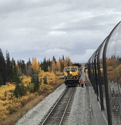 Two blue and yellow passenger trains on adjacent track exchanging crews.