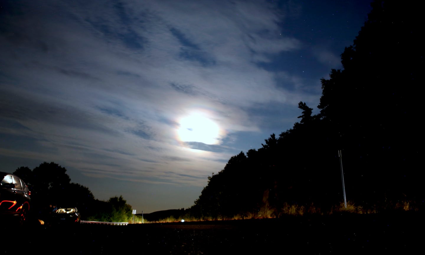 The moon shines over people parked at a scenic overlook to watch for aurora borealis in Alton Bay, N.H., as Canada and northern U.S. cities experienced moderate solar storms Thursday.