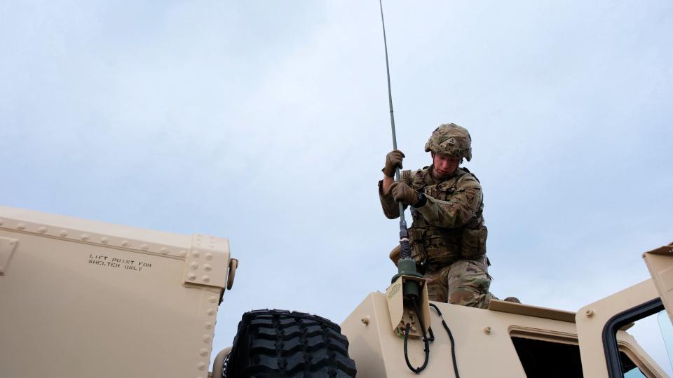 A US Army soldier attaches an atenna to the top of a Light Mobile Terrain Vehicle against a grey sky.