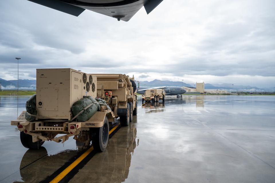 Two US Army Q-53 radar systems sit on a tarmac waiting to be loaded into plane against a grey sky.