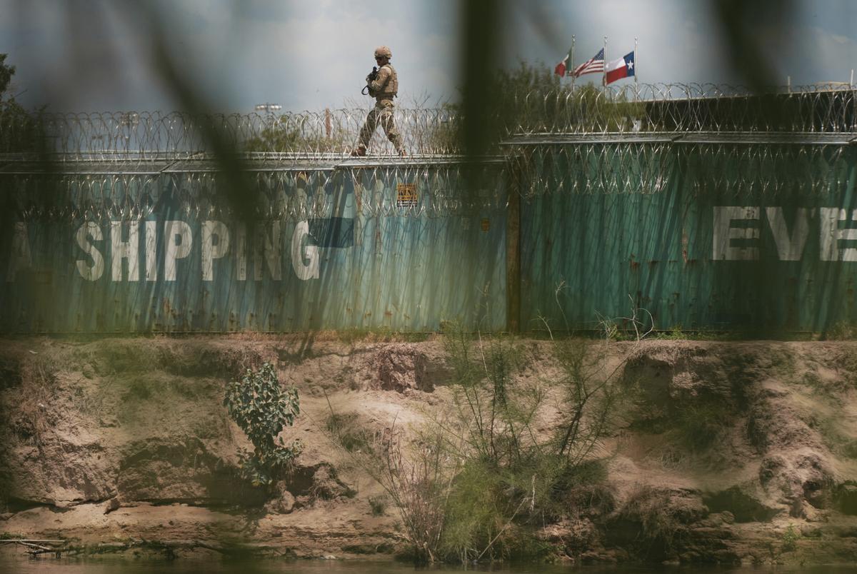 A member of the Texas Army National Guard patrols the Rio Grande from atop a line of shipping containers in Eagle Pass, Texas, on Friday, Aug. 9, 2024.