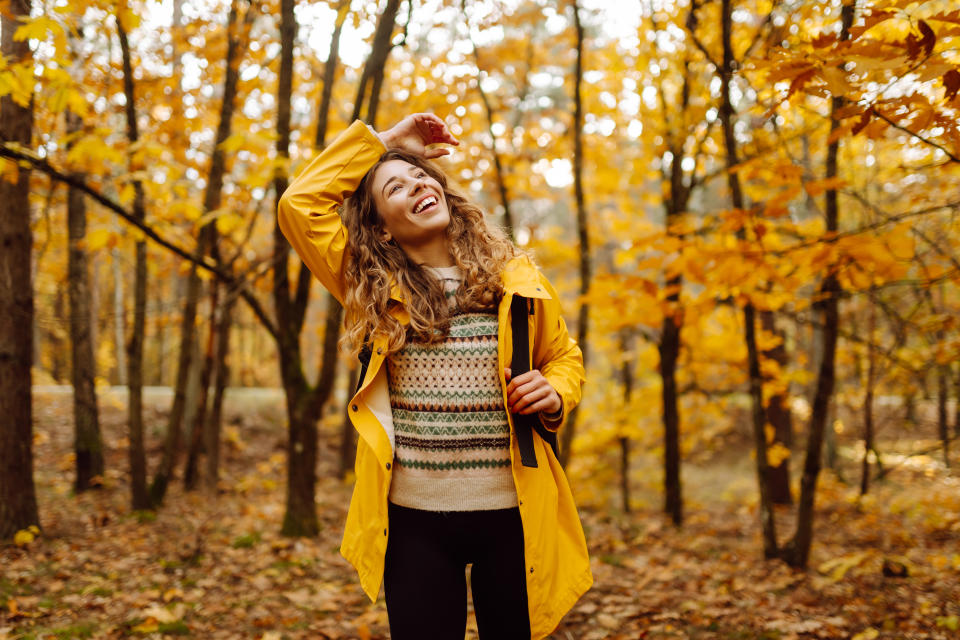 Young woman in a yellow raincoat exploring a vibrant autumn forest filled with colorful foliage during a sunny afternoon hike. Autumn landscape.