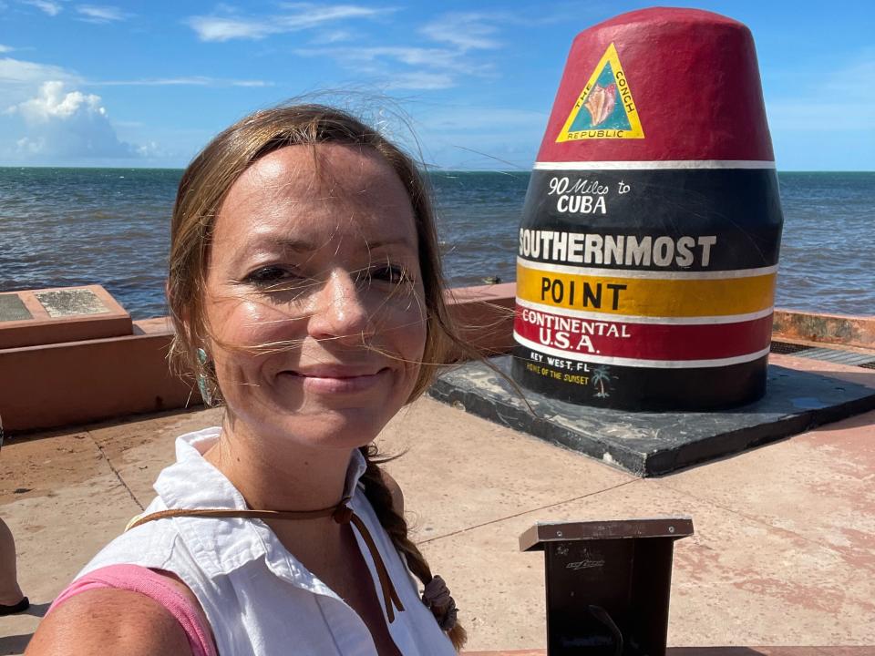 Emily taking a selfie in front of the Southernmost Point in Key West, Florida, with the ocean in the background.