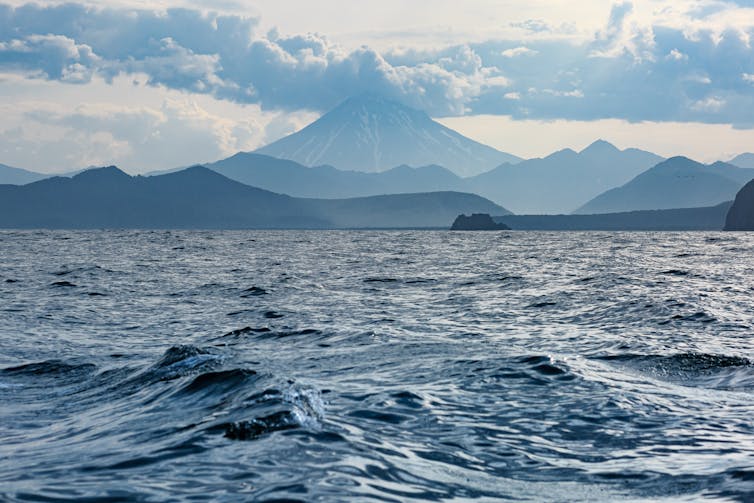 ocean with mountains and clouds in background