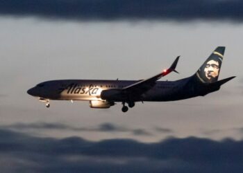 Alaska Airlines Boeing 737-800 landing at Ronald Reagan Washington National Airport during dusk, with building lights reflecting on the Potomac River