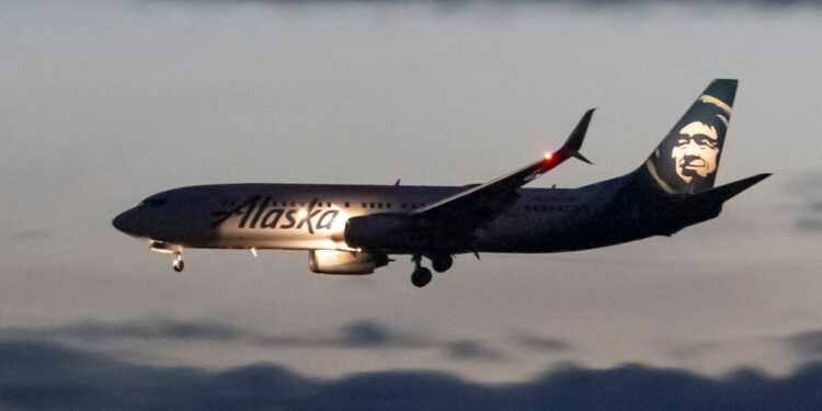 Alaska Airlines Boeing 737-800 landing at Ronald Reagan Washington National Airport during dusk, with building lights reflecting on the Potomac River