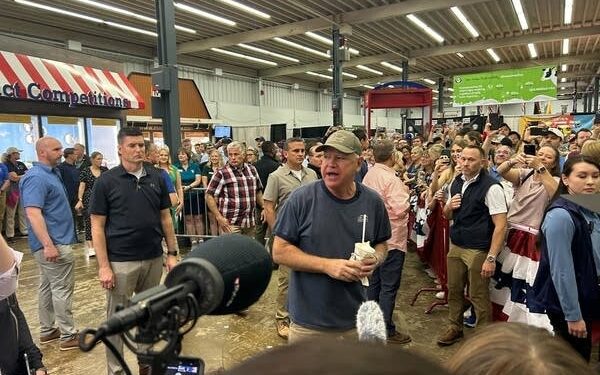 A man stands around a large crowd and media while speaking.