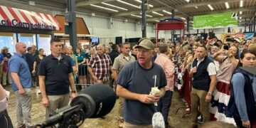 A man stands around a large crowd and media while speaking.