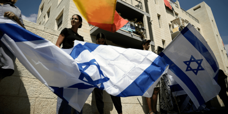 Mourners wave flags on the way to Hersh Goldberg-Polin's funeral (Leo Correa/AP)