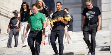 Boston Celtics Coach Joe Mazzulla, a Rhode Island native, walks down the Rhode Island State House steps with the NBA championship trophy along with Celtics co-owner Steve Pagliuca, left, and Rhode Island Governor Daniel J. McKee, right.