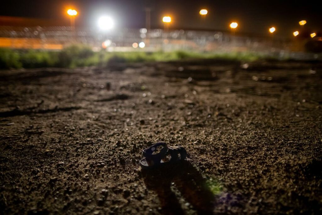 An abandoned baby sandal lies on the banks of the Rio Grande in Ciudad Juarez, Mexico with the razor wire and border wall of El Paso, Texas, in the background, late Thursday, Aug. 8, 2024.