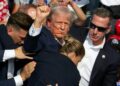 Republican candidate Donald Trump is seen with blood on his face surrounded by Secret Service agents as he is taken off the stage at a campaign event at Butler Farm Show Inc. in Butler, Pennsylvania, July 13, 2024. Donald Trump was hit in the ear in an apparent assassination attempt by a gunman at a campaign rally on Saturday, in a chaotic and shocking incident that will fuel fears of instability ahead of the 2024 US presidential election. (Photo by Rebecca DROKE / AFP)