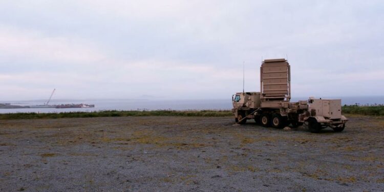 A US Army Q-53 Radar is parked on a sandy shore overlooking the ocean and a grey sky.