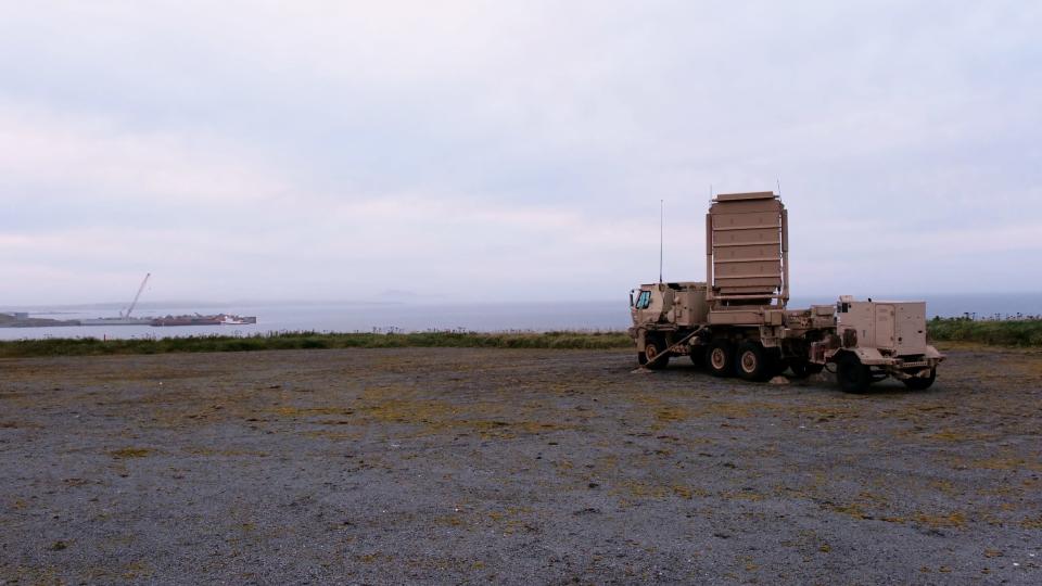 A US Army Q-53 Radar is parked on a sandy shore overlooking the ocean and a grey sky.