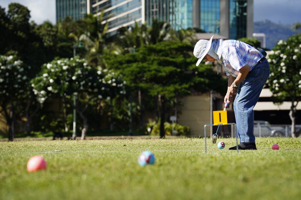 Gateball player Steven Kaneshiro strikes a ball toward the first gate during practice Wednesday, Sept. 4, 2024, at Ala Moana Beach Park in Honolulu. Kaneshiro discovered the sport after re-connecting with Art Kimura. Kimura was one of Kaneshiro’s high-school teachers. (Kevin Fujii/Civil Beat/2024)