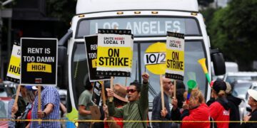 Hotel workers holding signs as they march and protest for their rights in Los Angeles, while a bus driver waits to cross the road, captured on October 25, 2023.